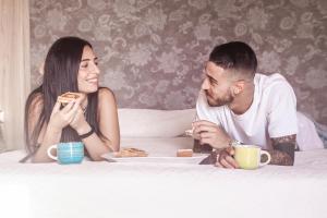 Um homem e uma mulher sentados numa cama a comer. em Agriturismo al Riparo dai Venti em Stintino