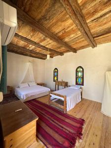 two beds in a room with wooden ceilings and windows at Beit Dina in Siwa