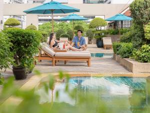 two people sitting on a couch next to a swimming pool at Grand Mercure Bangkok Atrium in Bangkok