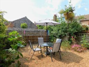 a patio with a table and chairs and an umbrella at 1 Orchard Cottages in West Runton