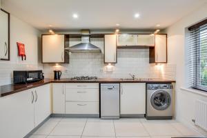 cocina con armarios blancos, lavadora y secadora en Elegant Bolton Abode - Sleeps 10, en Bolton