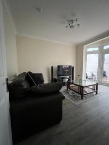 a living room with a black couch and a glass table at 4 Bedroom holiday home in Woodford