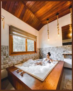a woman laying in a bath tub in a bathroom at Verde da Mantiqueira Chalés in Visconde De Maua