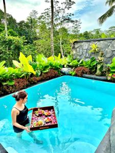 a woman holding a tray of food in a swimming pool at PONDOK KUNGKANG VILLA 2 in Ubud