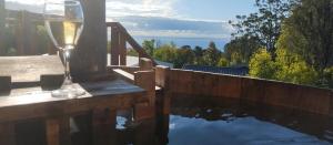 una copa de vino sentada en una mesa junto a un cuerpo de agua en Adilauquén Cabañas y Tinajas Calientes, en Puerto Varas 2 fotos más