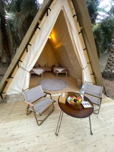 a tent with two chairs and a table in front of it at Husaak Glamping in AlUla