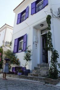 a woman standing in front of a white building with purple shutters at Amaranda Ada Evi in Bozcaada