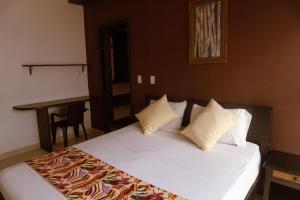 uma cama com lençóis brancos e almofadas num quarto em Tuki Hostel & Lounge em Pereira