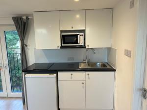a white kitchen with a sink and a microwave at Lovely Self Contained Loft Studio - 33AS4 in London