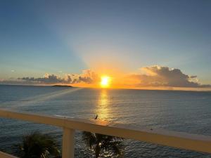a sunset over the ocean with a white railing at Hermoso Estudio frente al mar Ocean Blue Faith in Fajardo