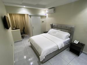 una camera da letto con un letto con lenzuola bianche e una TV di Emmaag Hotel, Ibadan a Ibadan