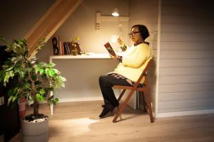 une femme assise sur une chaise en lisant un livre dans l'établissement Guesthouse in Manger, Radøy Island, à Kollstad