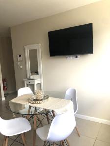 mesa de comedor con sillas blancas y TV en la pared en Gray Fox Apartments San Martin en Ushuaia