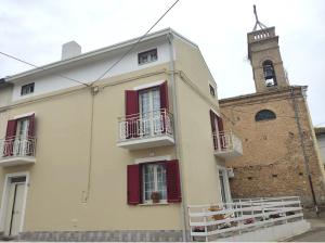 un edificio blanco con ventanas de contraventanas rojas y una iglesia en La casetta di Angela, en Lanciano