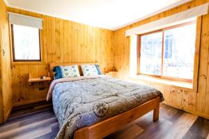 a bed in a wooden room with two windows at TERMAS DE CHILLAN Las Trancas in Chillán