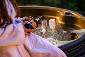 Una donna ha in mano una bottiglia di champagne e due bicchieri. di Forest Lodges a Betws-y-coed