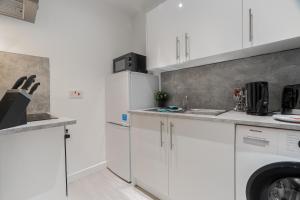 uma cozinha com armários brancos e uma máquina de lavar e secar roupa em Dyke Apartment em Uddingston