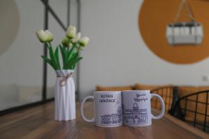 two coffee mugs sitting on a table with a vase of flowers at Kutaisi Heritage - Modern House in Historic District in Kutaisi