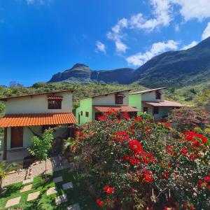 a row of houses with red flowers and mountains at Green Chales - Vale do Capão in Vale do Capao