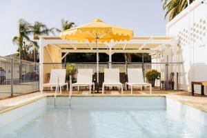 a swimming pool with an umbrella and chairs and a table and an umbrella at Port Broughton Hotel and Sunnyside Motel in Port Broughton