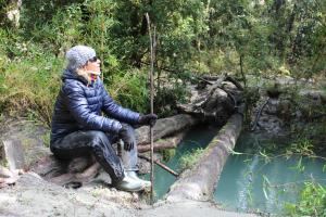 una persona sentada en un tronco junto a un cuerpo de agua en Alma Andina en Puelo