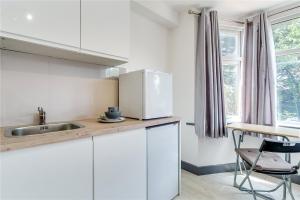 a white kitchen with a sink and a refrigerator at Modern Designer Studio Flat London in London