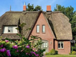 a thatched house with flowers in front of it at Reetdachhaushaelfte-1 in Sankt Peter-Ording