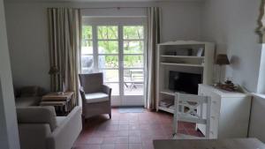 ein Wohnzimmer mit einem TV, einem Sofa und einem Stuhl in der Unterkunft Reetdachhaushälfte 1 in Sankt Peter-Ording