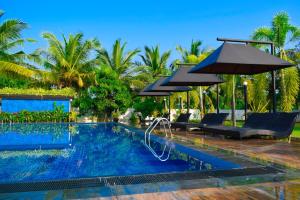 a swimming pool with an umbrella and chairs and trees at Hotel Green Garden in Trincomalee