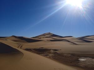 a desert with the sun shining over the sand dunes at Bivouac Liguera chez Ahmed in Mhamid
