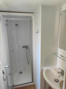 a white bathroom with a shower and a sink at Mobil-home in Valras-Plage