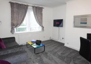 a living room with a couch and a table with a laptop at Welsh Drive Apartment by Klass Living Blantyre in High Blantyre