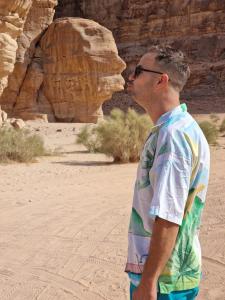 un hombre parado en el desierto besando una formación de roca en Adel rum camp bubbles, en Wadi Rum