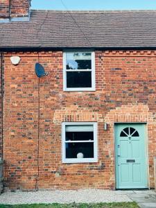 a brick building with a green door and two windows at 2 Cherry Tree Cottages in Stock