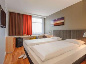 a hotel room with two beds and a desk at ibis Hotel Frankfurt Messe West in Frankfurt/Main