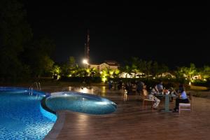 Corbett Selva Resort By DevStayZ في رامناجار: حمام سباحة في الليل مع أشخاص يجلسون حول الطاولة