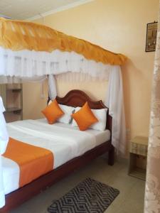 1 dormitorio con cama con dosel y almohadas de color naranja y blanco en Allamanda Gardens Resort en Nakuru