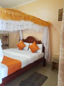 ein Schlafzimmer mit einem Himmelbett mit orangefarbenen und weißen Kissen in der Unterkunft Allamanda Gardens Resort in Nakuru