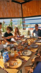 un grupo de personas sentadas alrededor de una mesa con comida en Good Wave Surf House en Tamraght Ou Fella
