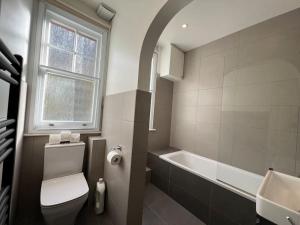 a bathroom with a toilet and a tub and a window at Star London Warwick Mansions 3-Bed Haven in London