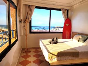 1 dormitorio con tabla de surf y 1 cama con ventana en Good Wave Surf House en Tamraght Ou Fella