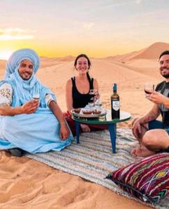 a group of people sitting in the desert with wine glasses at Overnight Desert Camp in Merzouga