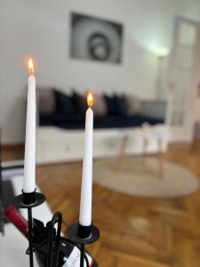 two white candles in a room with a wooden floor at Center Retro Apartment in Niš