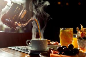 um bule de chá a despejar café numa chávena sobre uma mesa em Hotel Laghetto Stilo Borges em Gramado