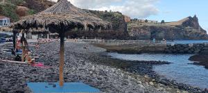 een strand met een strooien parasol op een rotsachtige kust bij Reis Magos Beach Caniço Sea line Apartment in Caniço