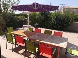 een houten tafel met kleurrijke stoelen en een parasol bij Charmante villa d.Architecte 200m2 à 20 min de la mer in Saint-Geniès-de-Fontedit