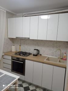 una cucina con armadi bianchi, piano cottura e lavello di Apart.Botanica a Chişinău Altre 12 foto