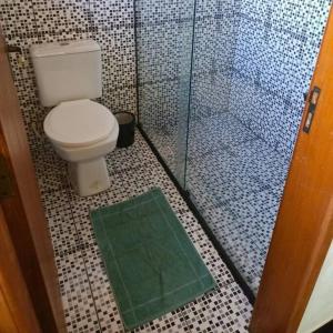 y baño con aseo y ducha con alfombra verde. en Sítio Vale dos Reis, en Resende