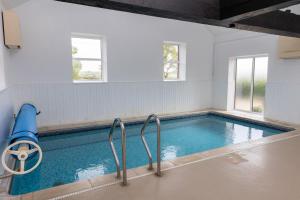 a swimming pool with blue water and two windows at Halcyon Cottage in Little Torrington