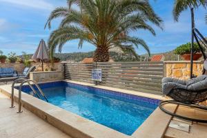 a swimming pool with two chairs and palm trees at Villa Capitis in the center-Deluxe Apartment with Swimming Pool in Hvar